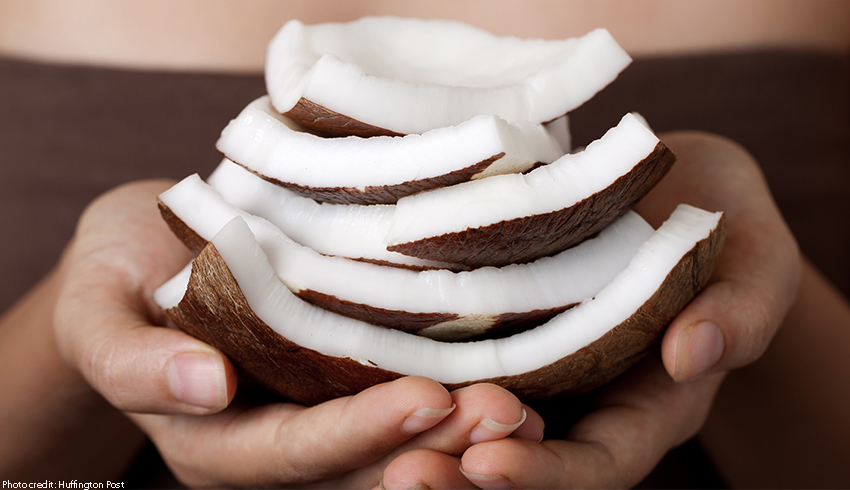 A woman holding pieces of coconut with shell intact in the palms of her hands.